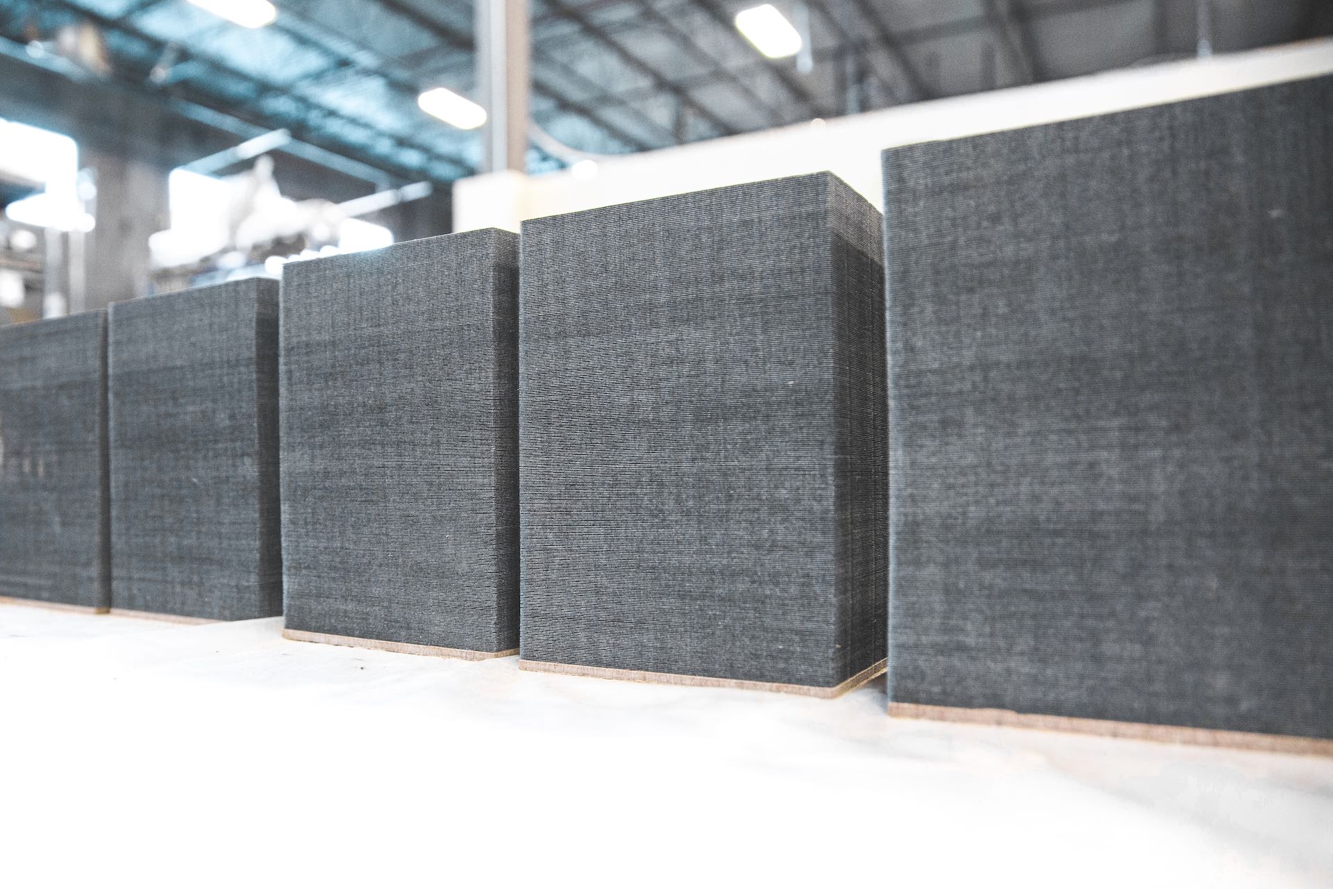 A row of grey cube-shaped filter units sits on a white floor, against a white knee-wall in an industrial building.