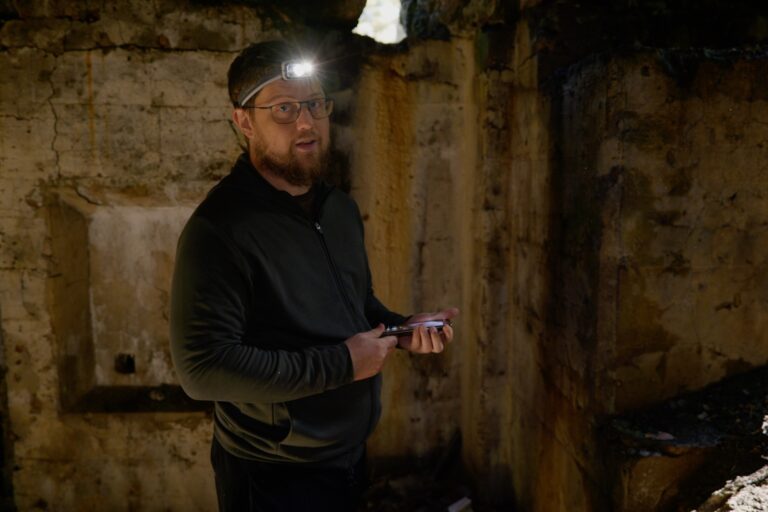 Software developer Peter Todd wearing a headlamp, standing in a dimly lit mining structure, and holding a flashlight.