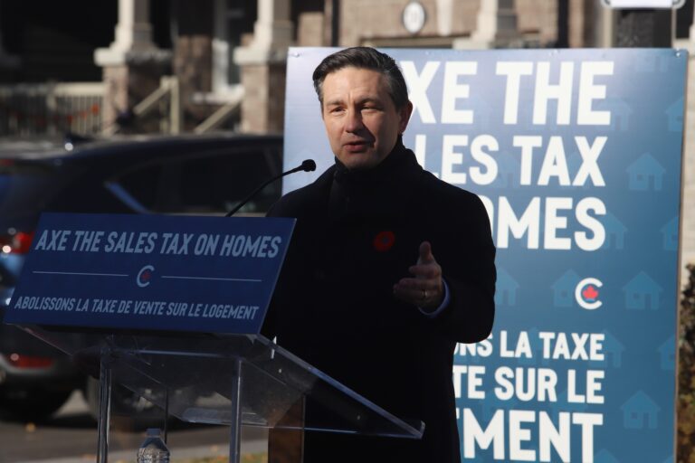 Conservative leader Pierre Poilievre standing behind a lectern with signs advocating for axing the sales tax on homes.
