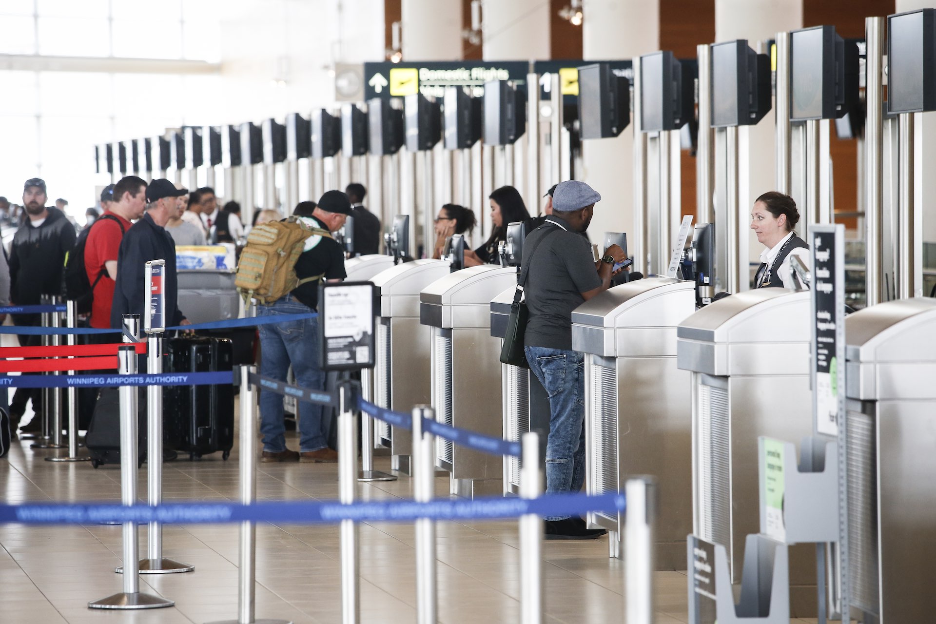 Travellers pass through a row of stainless-steel turnstiles at an airport as a Canada Border Services official looks on.