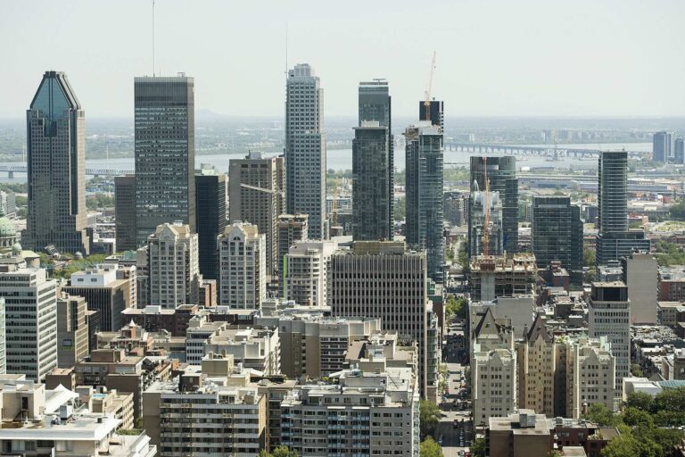 Skyline of Montreal city with numerous high-rise buildings and a bridge in the background under a clear sky.