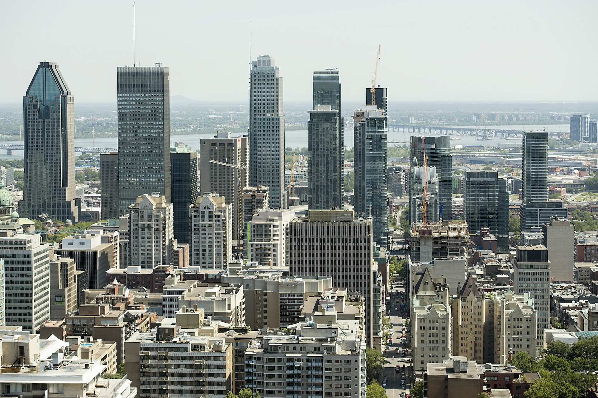 Skyline of Montreal city with numerous high-rise buildings and a bridge in the background under a clear sky.