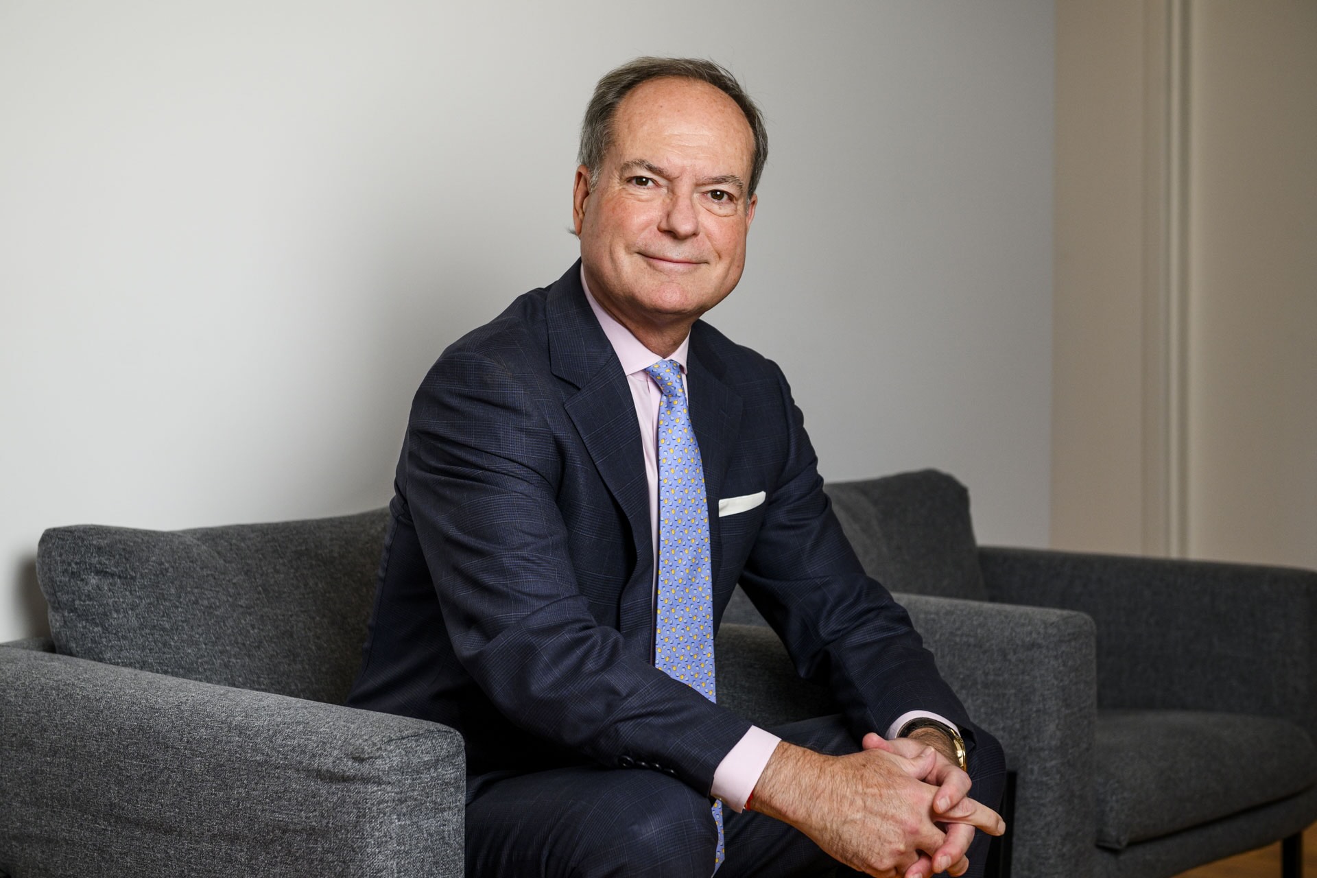 Ontario Minister of Finance Peter Bethlenfalvy in a suit sitting on a grey couch against a plain background.