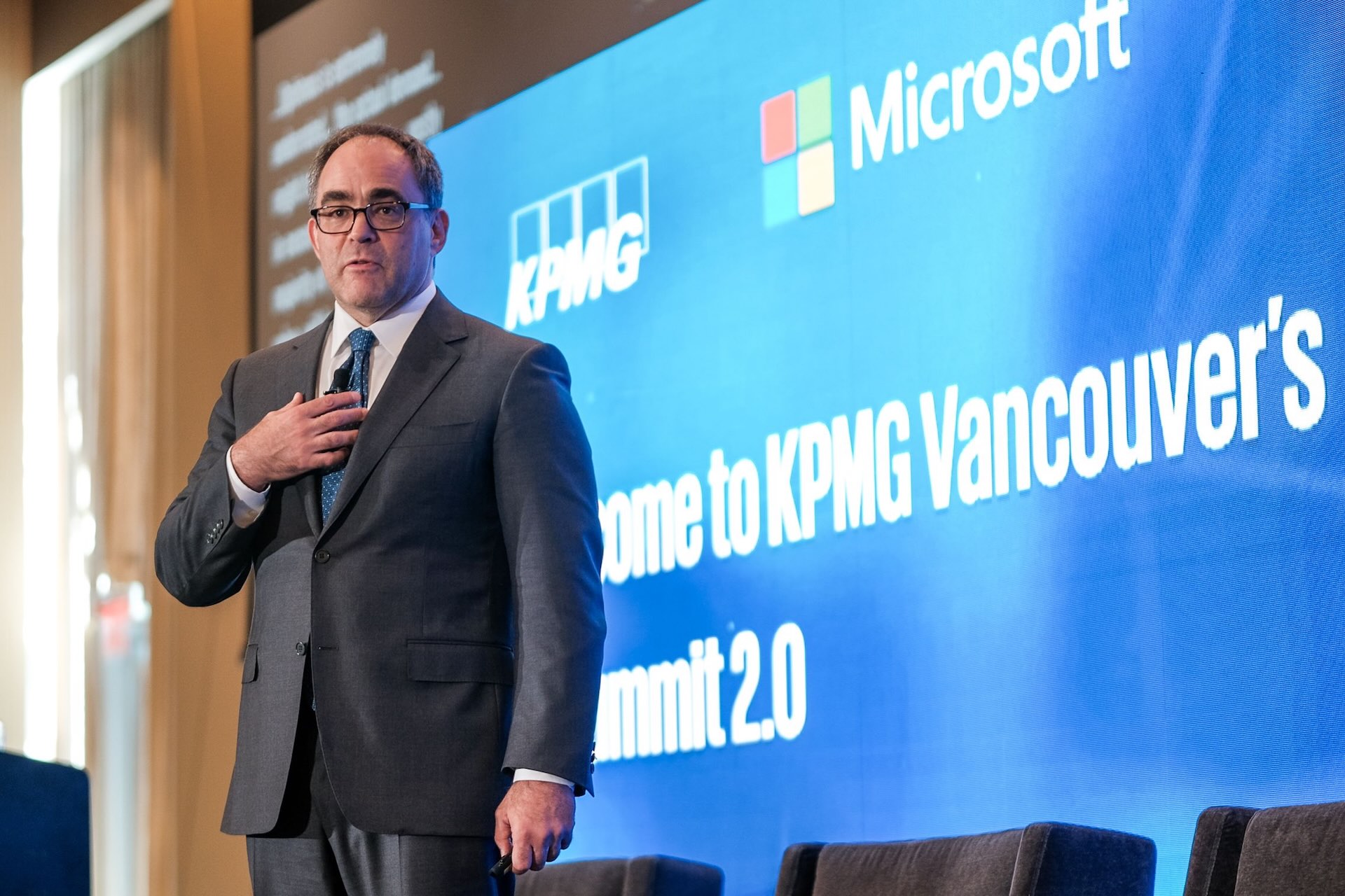 Sanctuary AI former CEO Geordie Rose in a suit standing on stage near a screen displaying KPMG, Microsoft logos, and “Welcome to KPMG Vancouver’s Summit 2.0”.