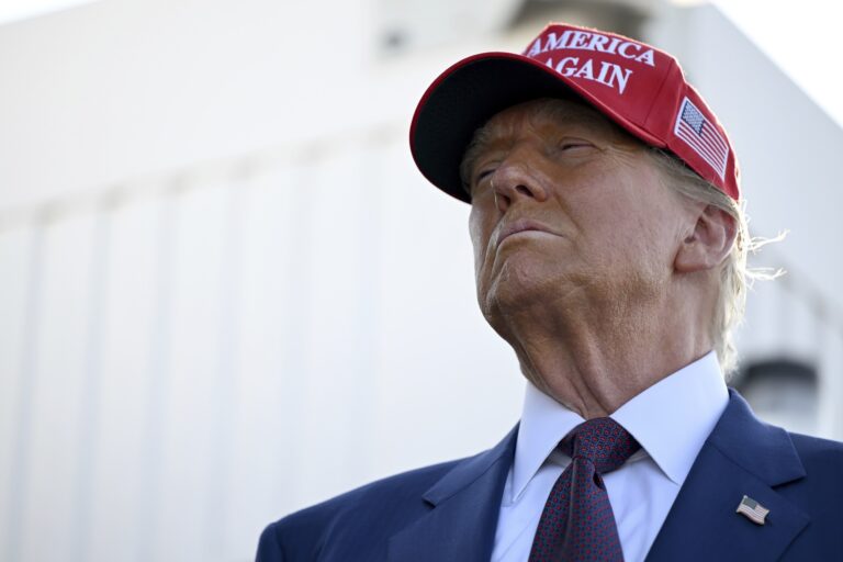 U.S. president-elect Donald Trump wearing a red hat with the words "Make American Great Again" visible and a blue suit with an American flag pin on his shoulder.