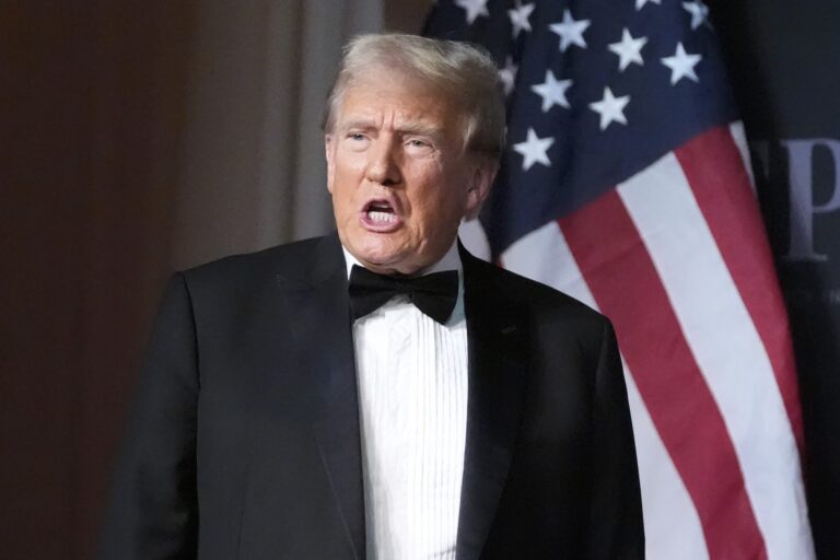 U.S. president-elect Donald Trump in a tuxedo speaking in front of a U.S. flag backdrop.