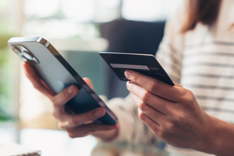 Person holding a smartphone in one hand and a credit card in the other, indicating online payment or shopping activity.