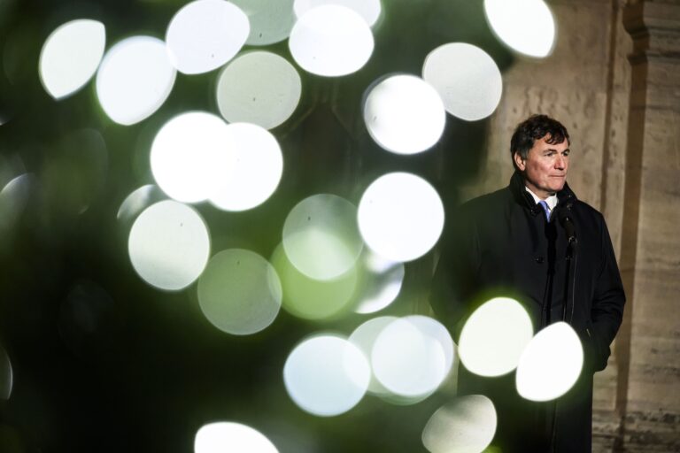 LeBlanc stands with his hands in the pockets of a dark jacket on the right side of the frame. The stonework of Rideau Hall can be seen in the background; in the left foreground are blurred Christmas lights on a tree on the Rideau Hall grounds.