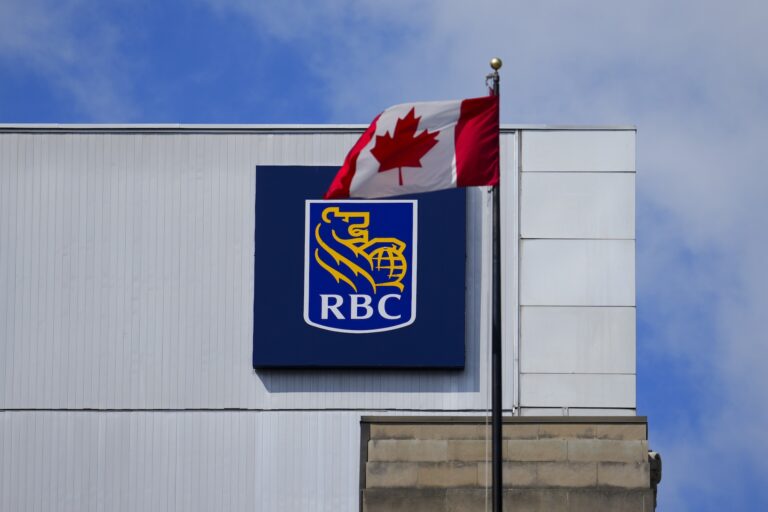 A Canadian flag flies in front of a building with an RBC logo on a blue sign.