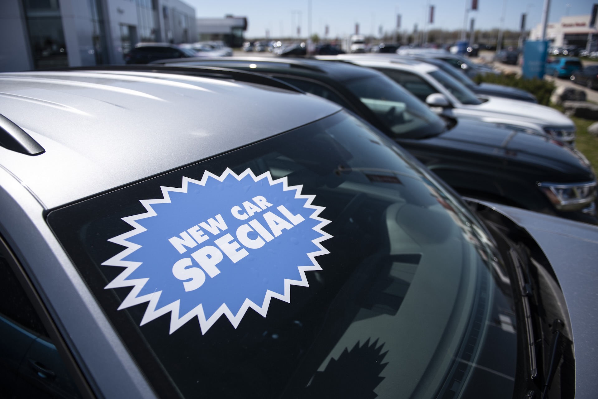 A shot of the windshield of a grey SUV on a car lot. On it is a large, blue sticker reading "New car special."
