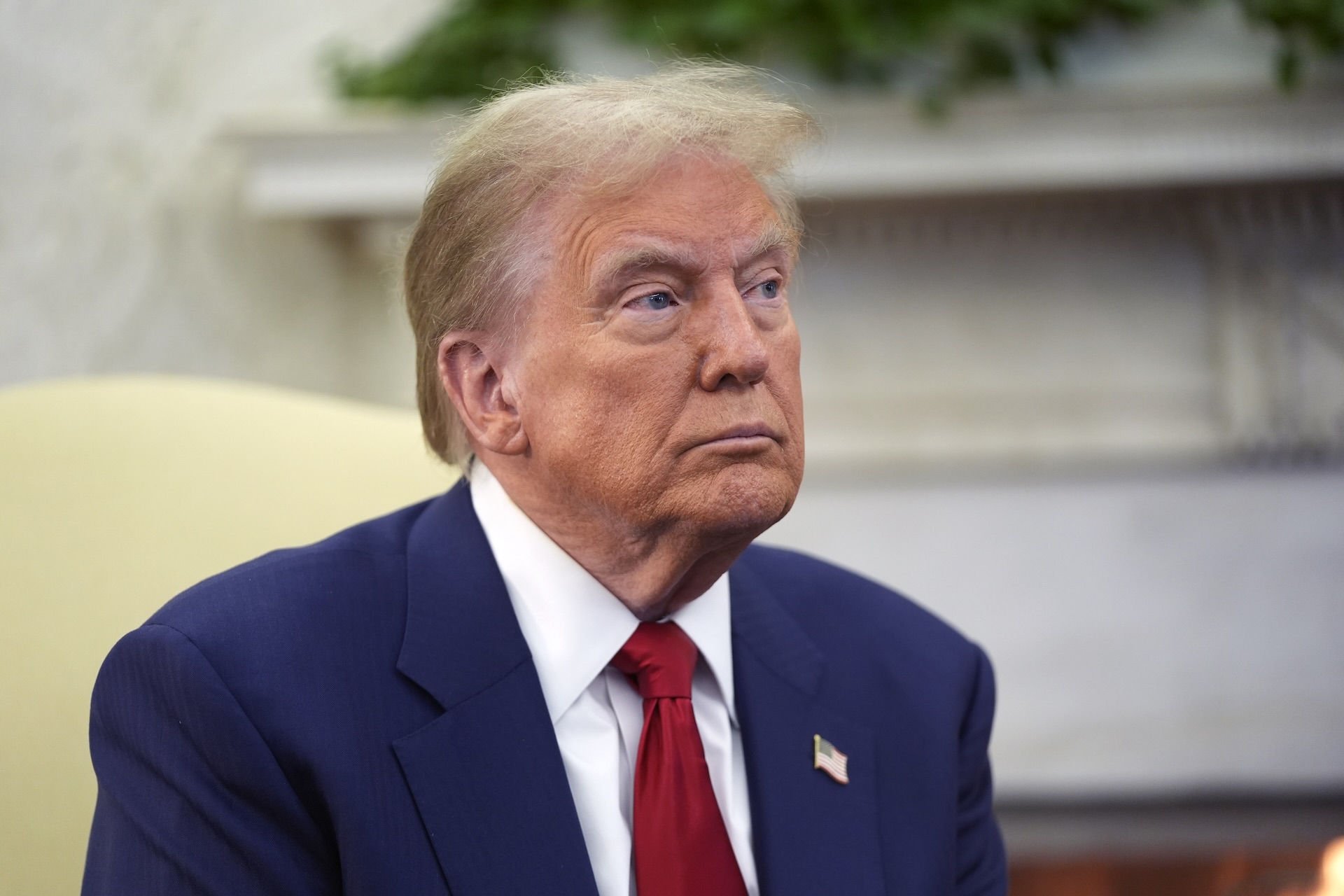 A photo of Donald Trump in a blue suit and red tie with the White House’s Oval Office in the background.