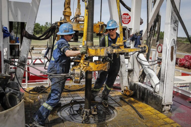 Two workers at an oil rig. A red sign behind them says, "STOP BEWARE OF DANGER ZONE."