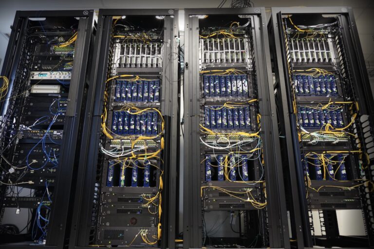 Close-up of four large computer bays with numerous blue and yellow wires running between various components.