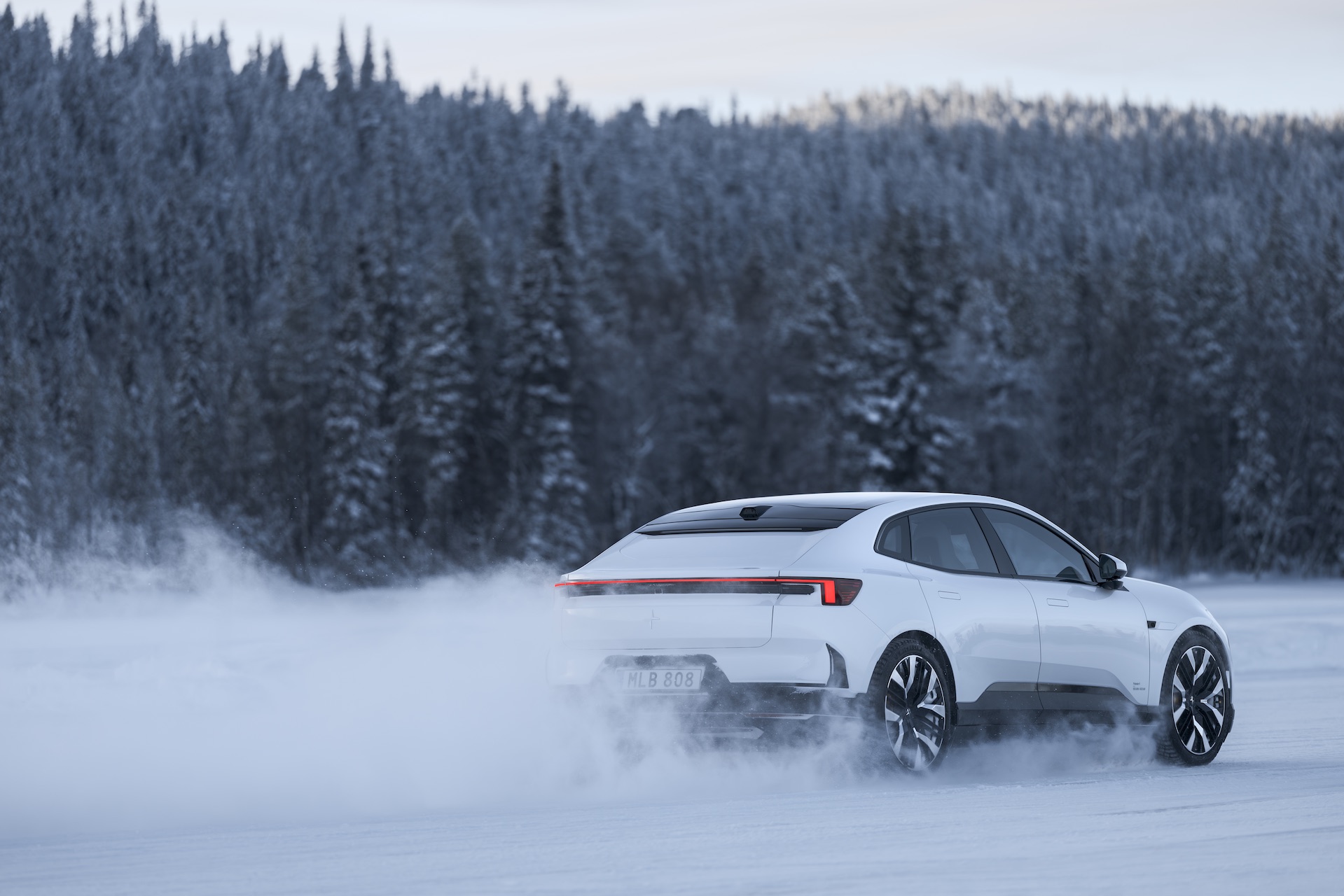 A sleek white vehicle driving across a frozen lake, with a backdrop of trees and snow billowing behind it.