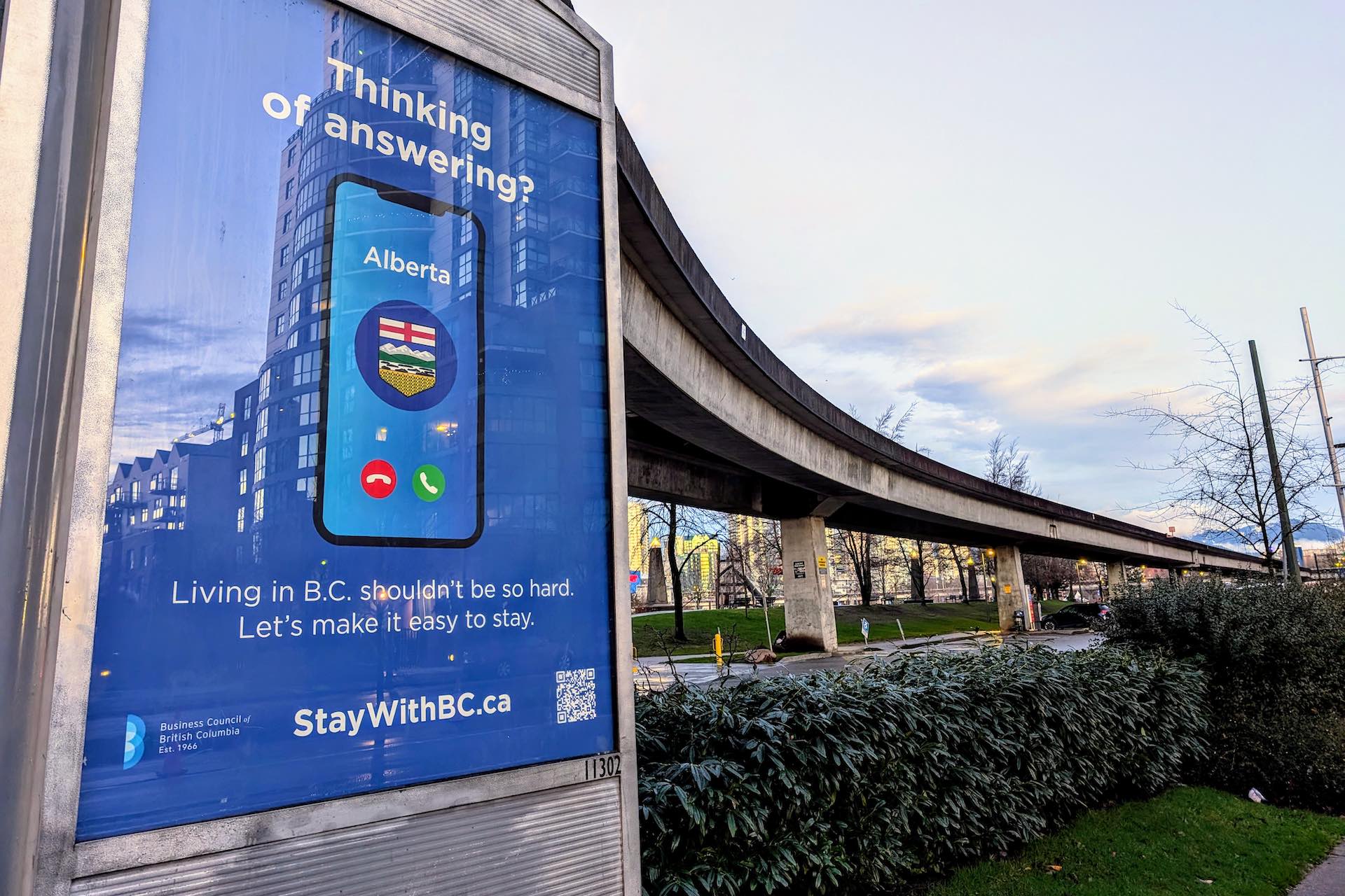 A shot of a bus-shelter poster along the SkyTrain's elevated tracks in Vancouver. The ad shows a picture of a phone with an incoming call from "Alberta." The wording on the ad asks, "Thinking of answering?"