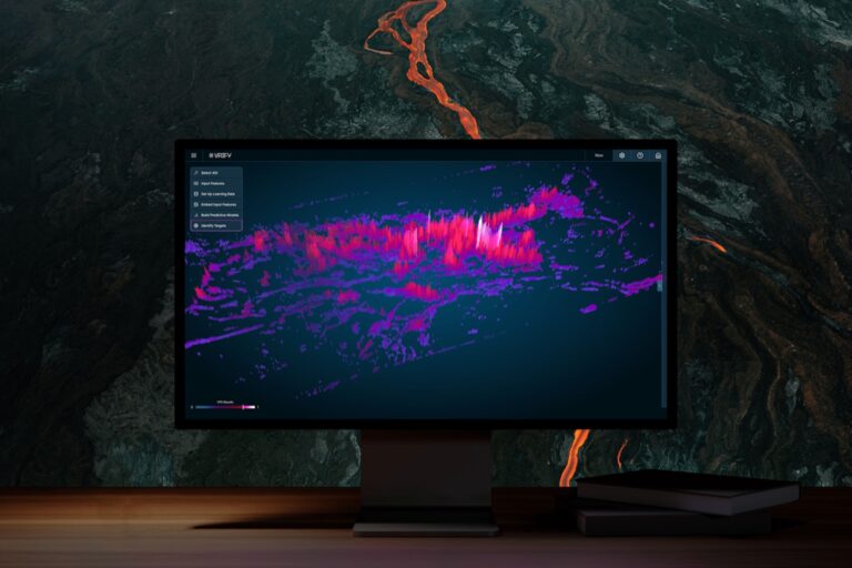 A monitor screen shows a rendering of a topographical map with pink and purple spikes on a black background. Behind the monitor is a backdrop of a stone wall.