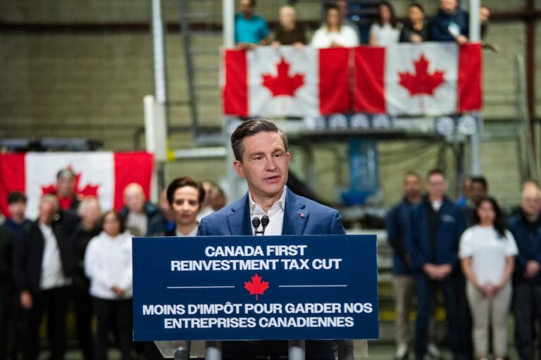 Conservative Leader Pierre Poilievre speaking with the words “Canada First Reinvestment Tax Cut” on the podium and Canadian flags behind him.