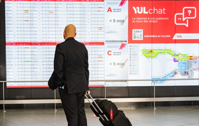 A traveller in a black suit looks at an airport’s arrival and departure board at Montreal-Pierre Elliott Trudeau International Airport in Montreal.