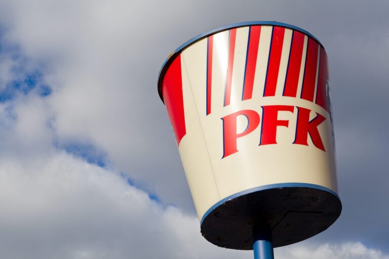 Large red and white PFK bucket sign against a cloudy blue sky.