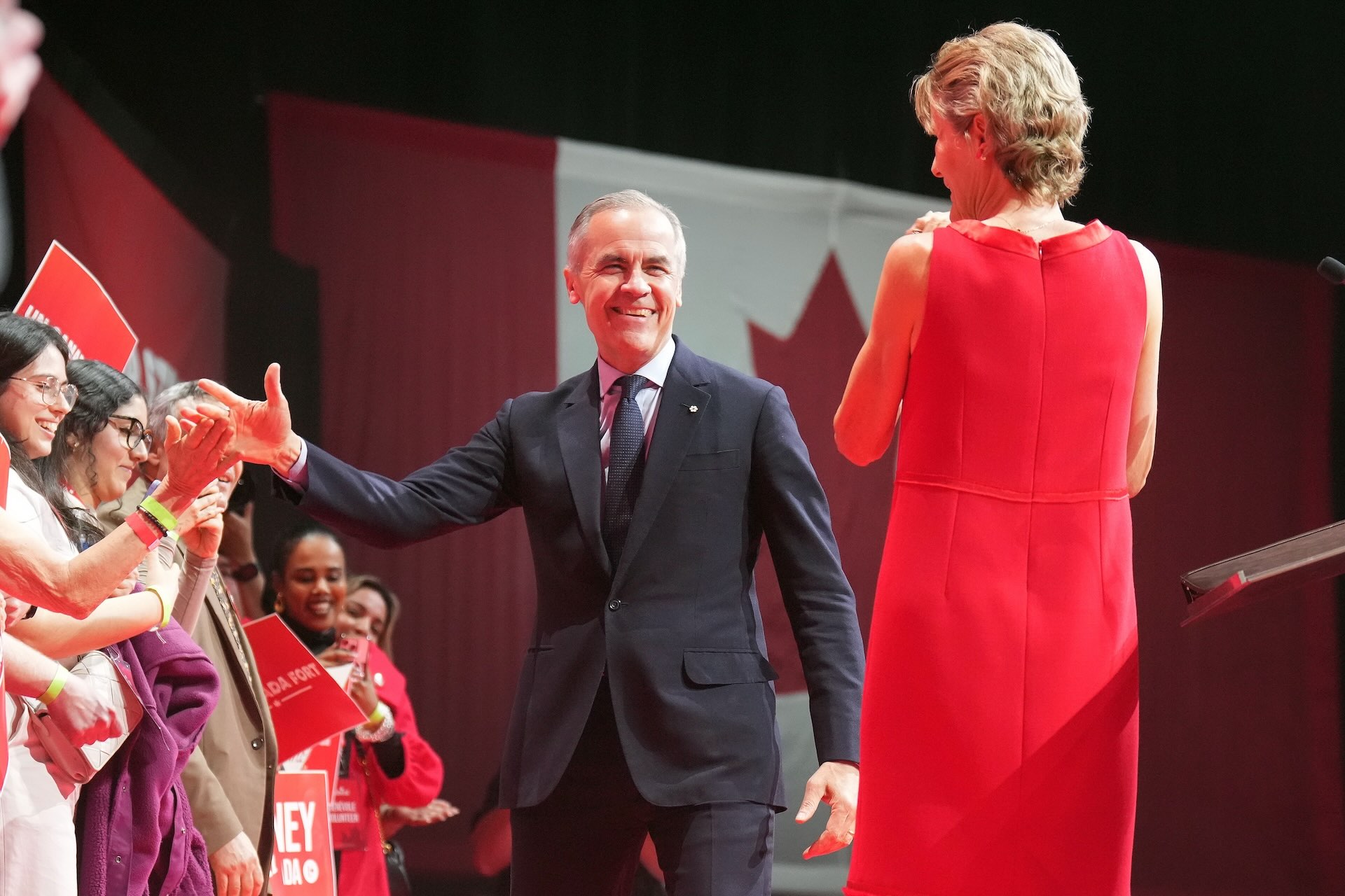Canadian Prime Minister Mark Carney high-fives his supporters on stage in front of a Canadian flag with his wife, Diana Fox Carney.