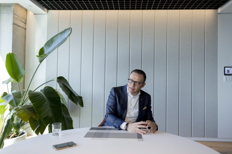 Guy Cormier, CEO and president of Desjardins, gestures with his hands while seated at a table with a plant to his left.