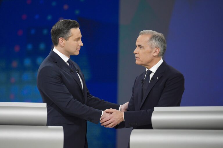 A shot taken during the 2025 election debate of Pierre Poilievre shaking hands with Mark Carney. Poilievre is holding Carney's elbow with his free hand, and Carney is shaking Poilievre's hand with both of his.