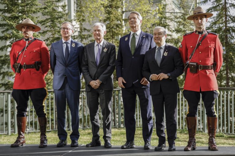 A posed shot of the respective finance ministers and central bank governors of Canada and the United States. They're standing in a row on a dais, flanked on each end by a Mountie in formal red serge and Stetson hat.