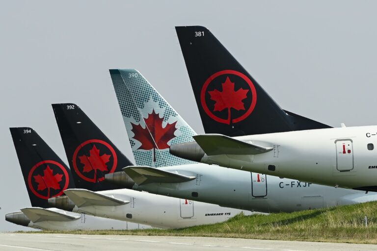 Four Air Canada aircraft are lined up on the tarmac, showing their tail fins with the airline's red maple leaf logo.