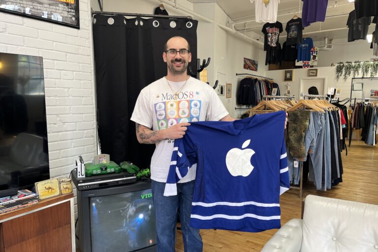 Nicholas Malisani poses while holding up a blue-and-white jersey with an Apple logo on the front in his pop-up store in downtown Toronto.