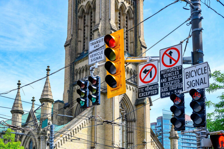 A cluster of car- and bicycle-traffic signals hanging over a street, with a large church steeple in the background.