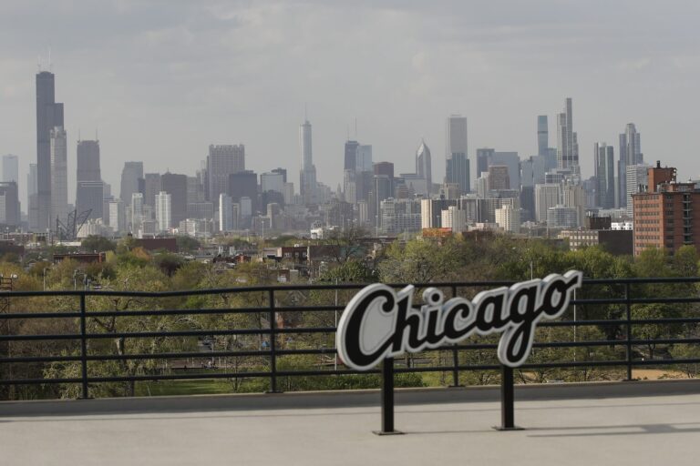 View of the Chicago skyline with skyscrapers in the background and a sign reading "Chicago" in the foreground.