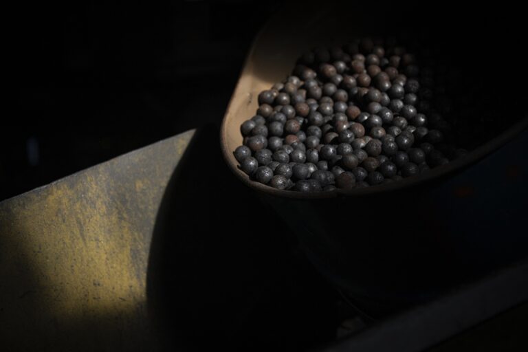 A close-up of a metal bin filed with balls of black and rust-coloured graphite.