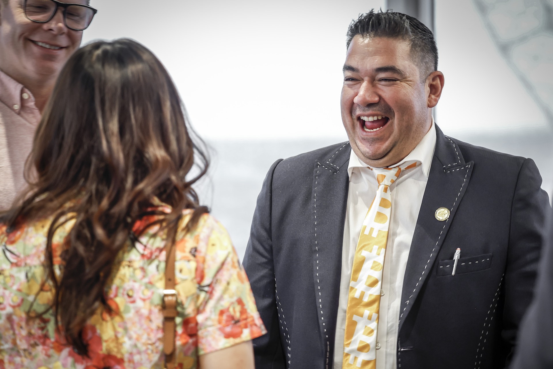 A shot of Juan Carlos Reyes laughing heartily, taken over the shoulder of the woman to whom he's speaking.