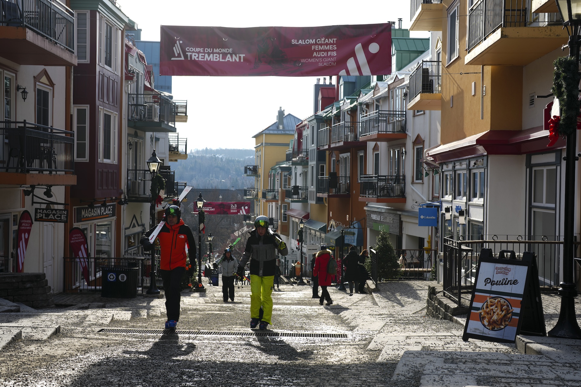 People walk through a ski village with shops and apartments on the left and right