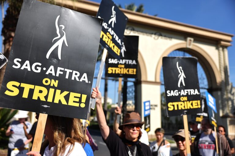 Picketers hold signs that read "SAG-AFTRA ON STRIKE!" outside a building with a large archway that says "Paramount Pictures."