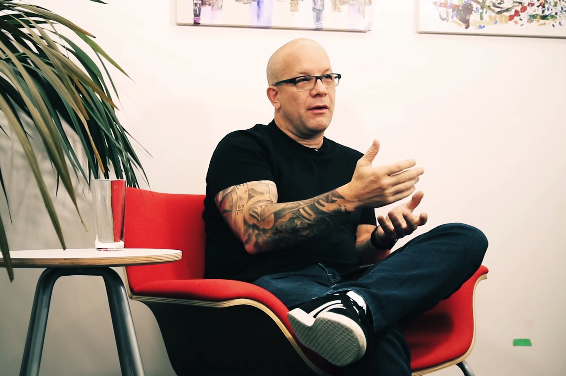 A shot of Scott Gravelle speaking while seated in a red chair. He’s wearing jeans, sneakers and a tight black shirt.