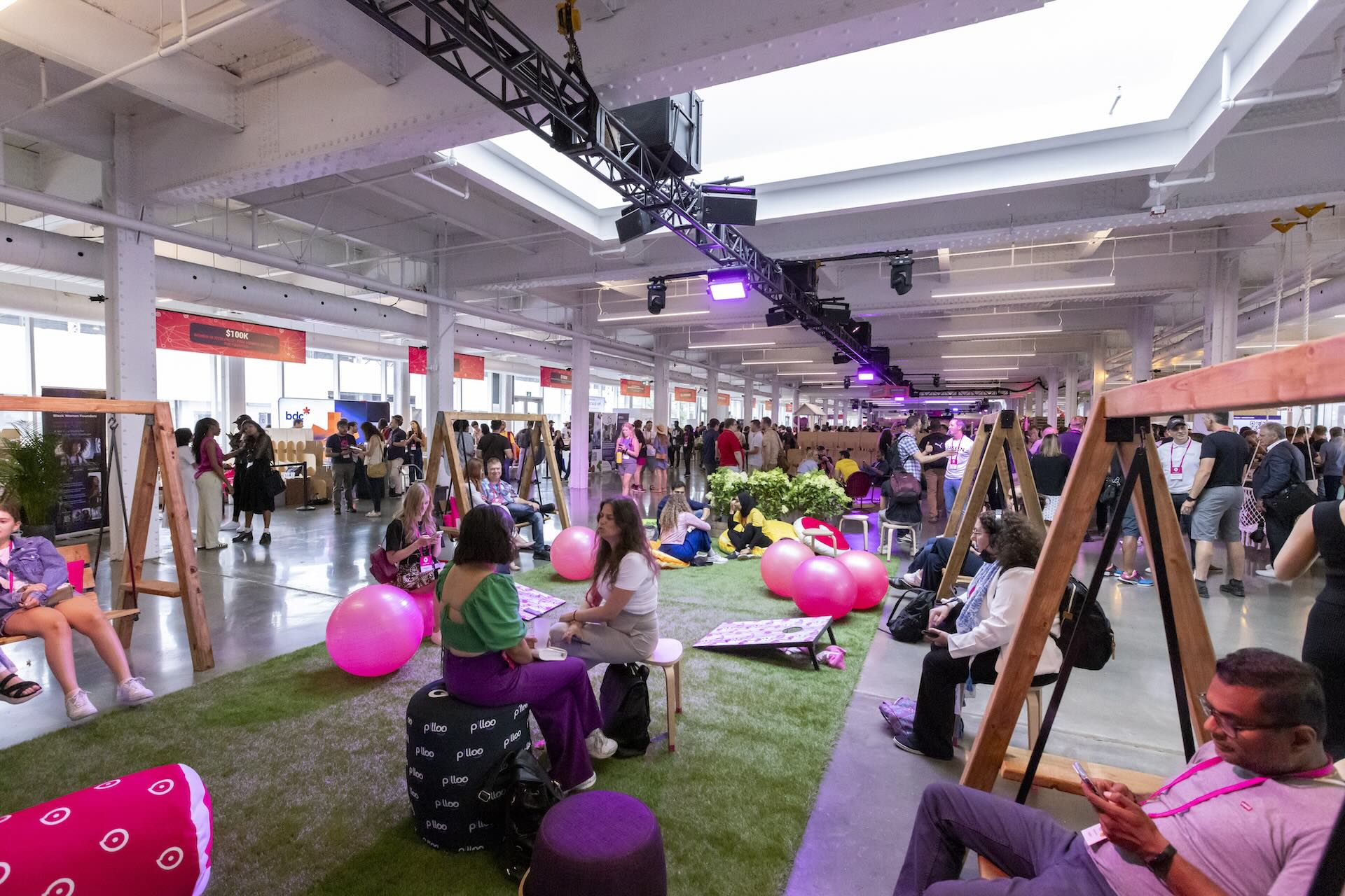 An image from Startupfest in Montreal with a convention hall split down the middle by a strip of artificial grass with wooden swings, balloons, and stools for attendees to sit.