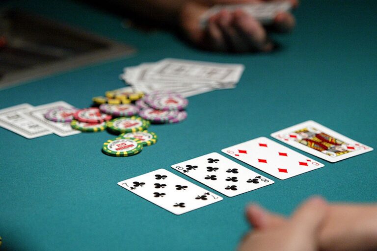 Four playing cards and a pile of chips are laid out on a blue table in a casino.