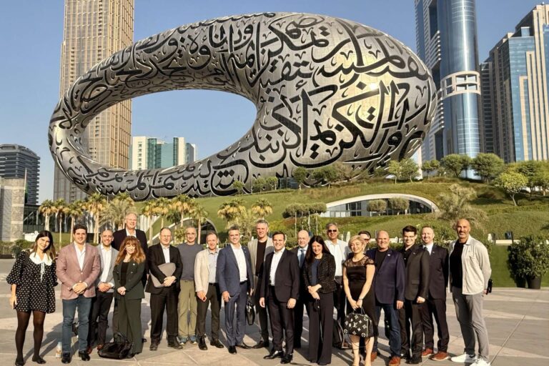 A group of people stands smiling in front of the Museum of the Future in Dubai. The futuristic, oval structure is adorned with Arabic calligraphy.