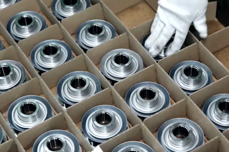 A close-up of silver-coloured, finely machined autoparts being packed into a box.