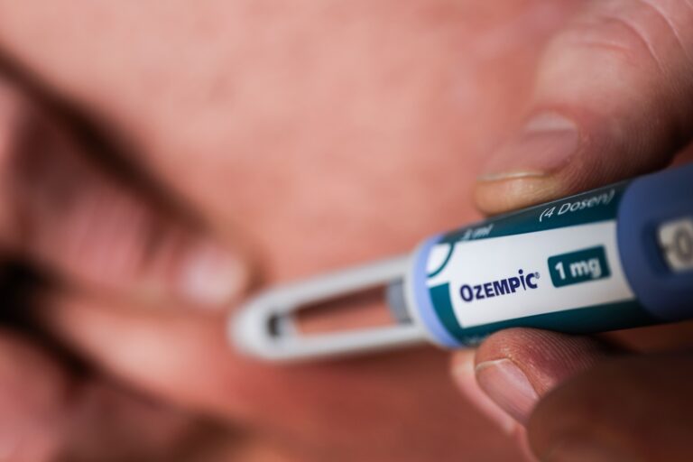 A closeup of a person using a pen-style syringe to inject Ozempic. The syringe is in focus in the foreground.