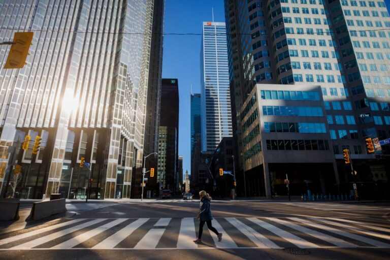 A person crosses the street on a painted crosswalk with a downtown background of grey, reflective skyscrapers.