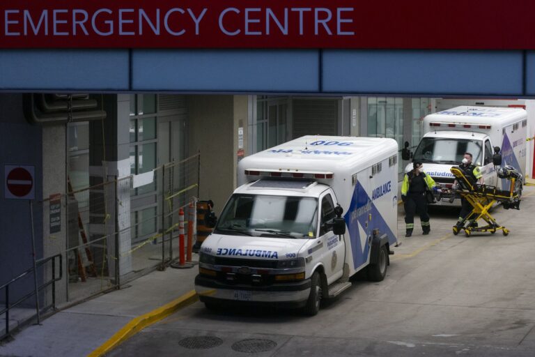 Paramedics moving equipment at an emergency room entrance. There are two ambulances parked by the entrance.