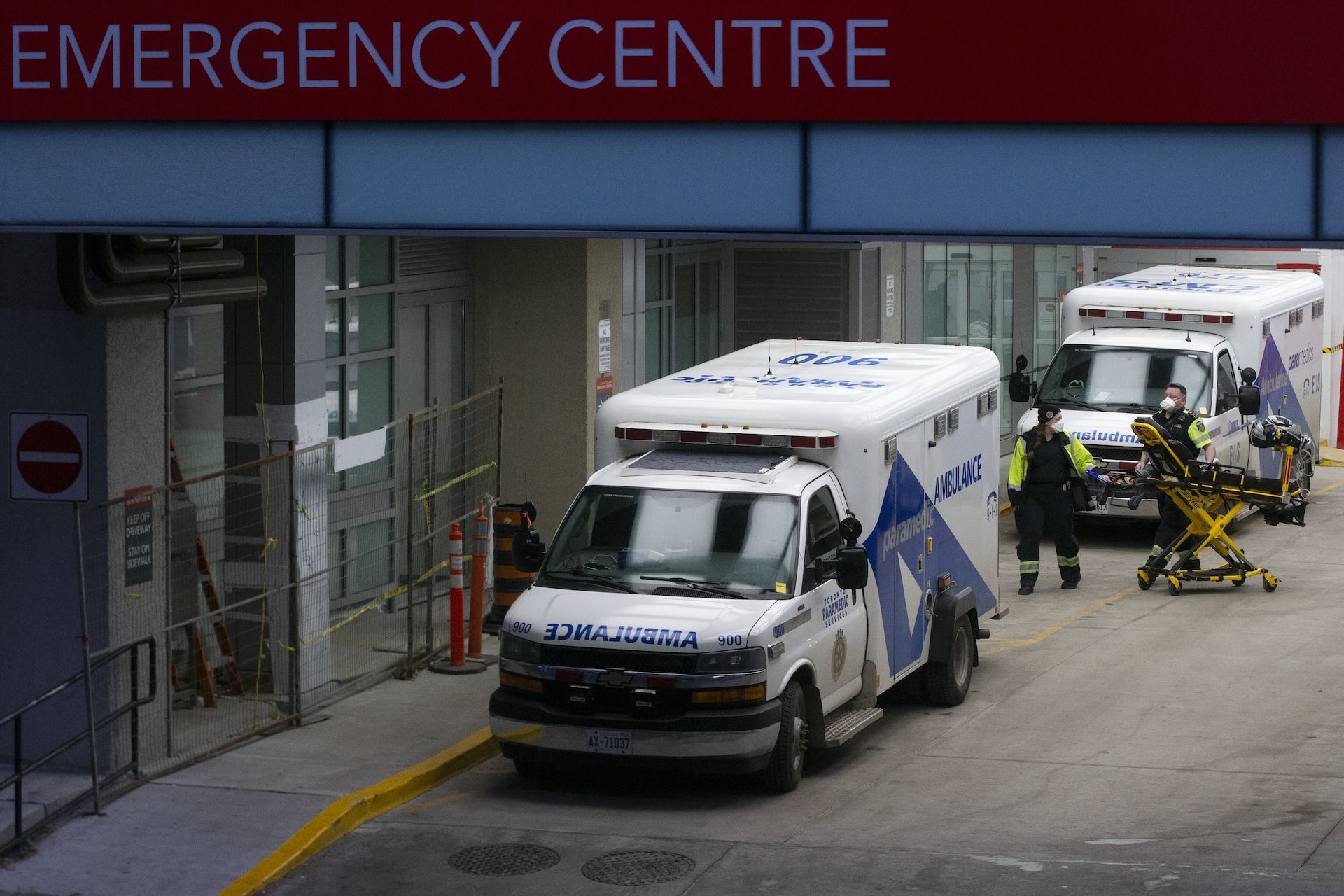 Paramedics moving equipment at an emergency room entrance. There are two ambulances parked by the entrance.