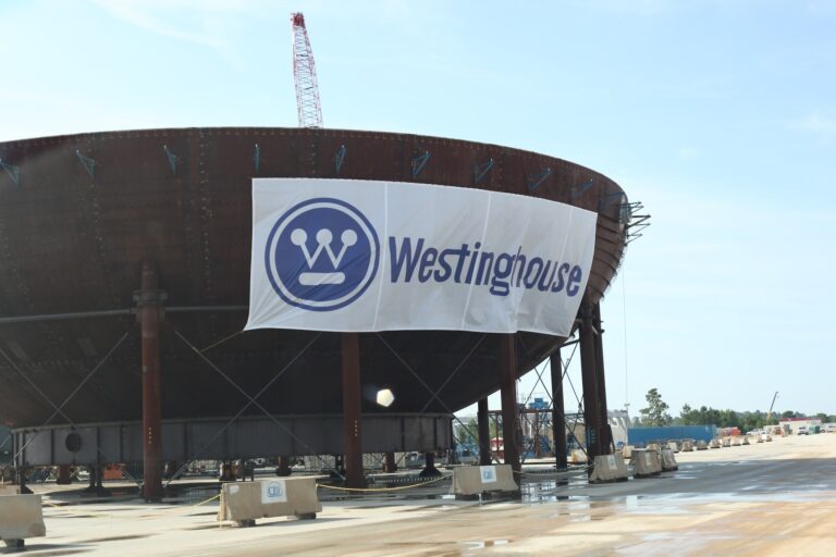 A bowl-shaped structure surrounded by concrete barriers. A white sign with a blue Westinghouse logo is suspended across one side of the structure.