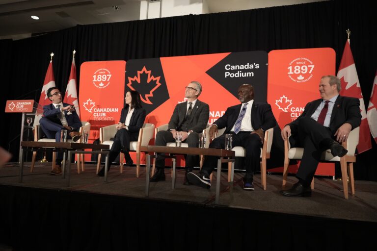 A wide shot of panellists onstage at a Canadian Club Toronto event.