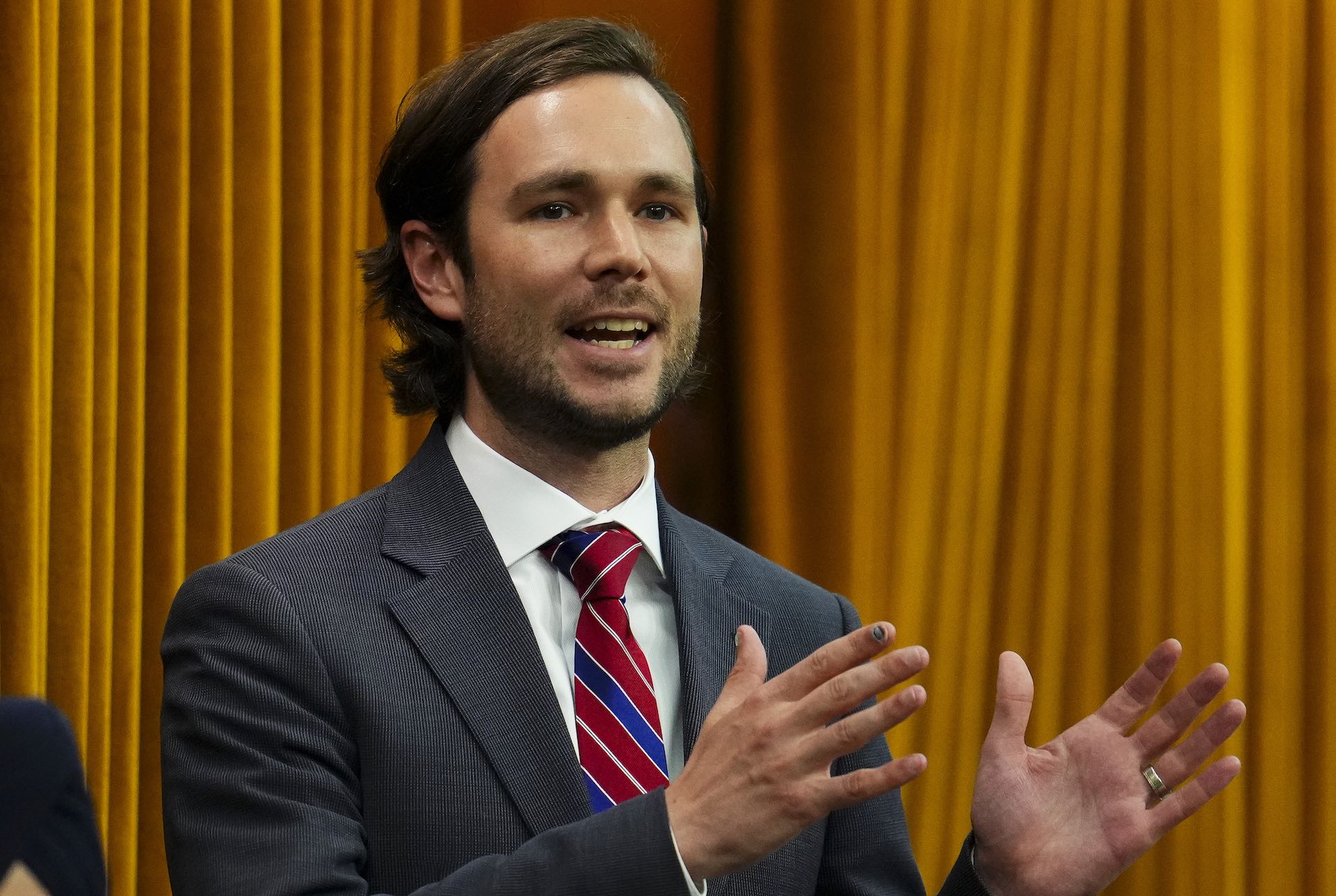 A head-and-shoulder shot of Jacob Mantle speaking in the House of Commons. The curtain behind the benches is in the background.