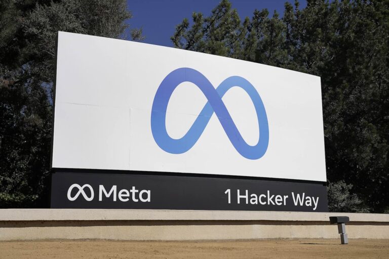 A large sign with Meta's blue ouroboros-like "M" logo on a white background. The company name and address "1 Hacker Way" is listed along the bottom edge of the sign.