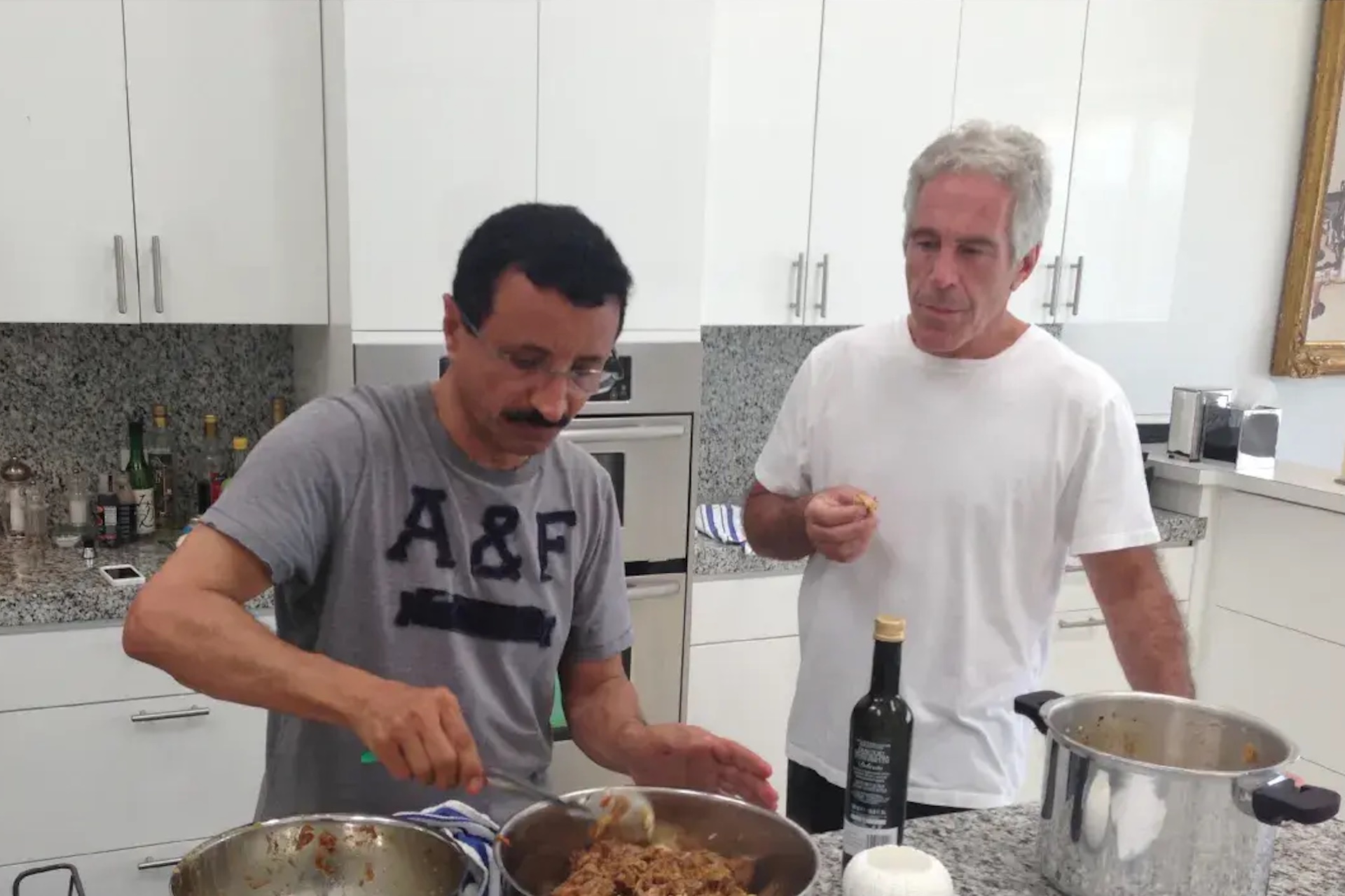 A shot of Sultan Ahmed bin Sulayem in casual wear cooking in a kitchen, with Jeffrey Epstein standing to his left in a white t-shirt.
