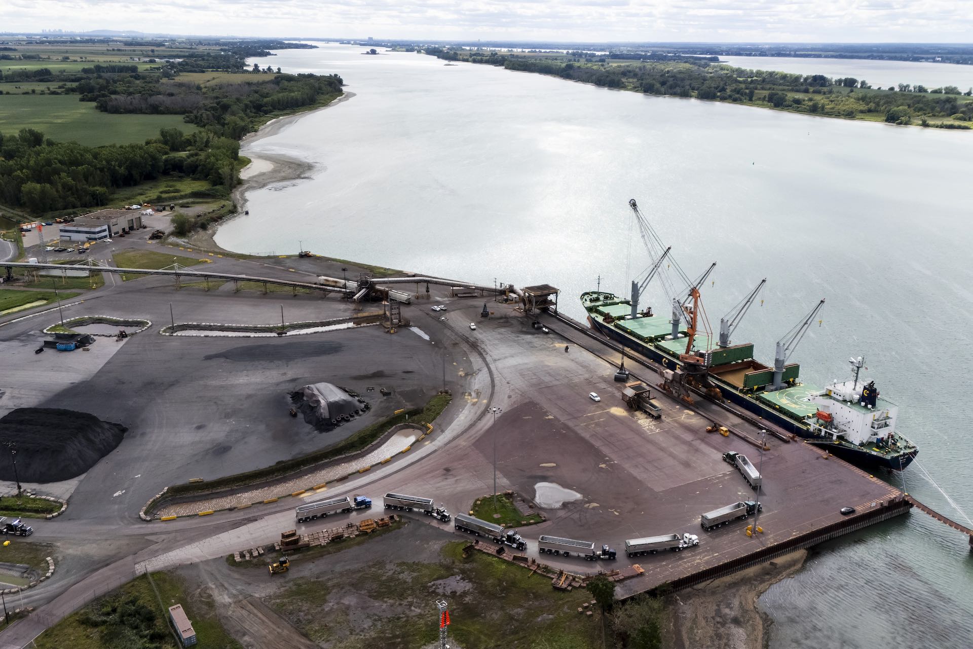 An aerial shot of a port facility on the St. Lawrence River, with a ship docked and transport trucks lined up to meet it.